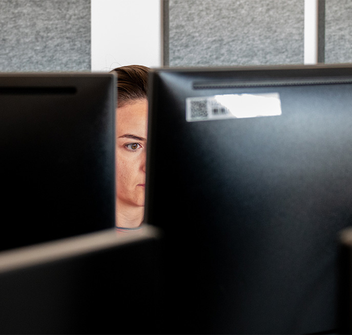 long haired person working at a computer seen through two computer screens (Photo)